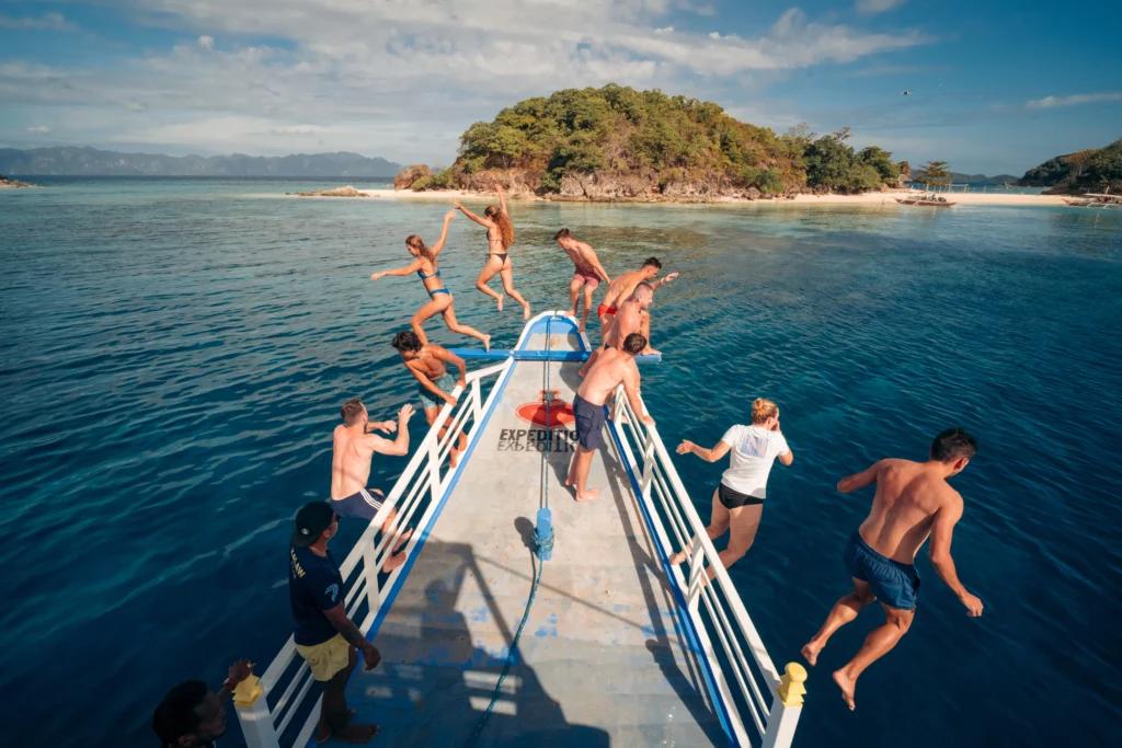 Travelers jumping off the bow of a boat into crystal clear waters during a 3-day Palawan island hopping adventure.