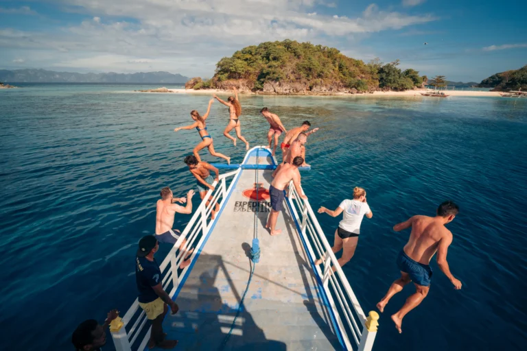 Travelers jumping off the bow of a boat into crystal clear waters during a 3-day Palawan island hopping adventure.