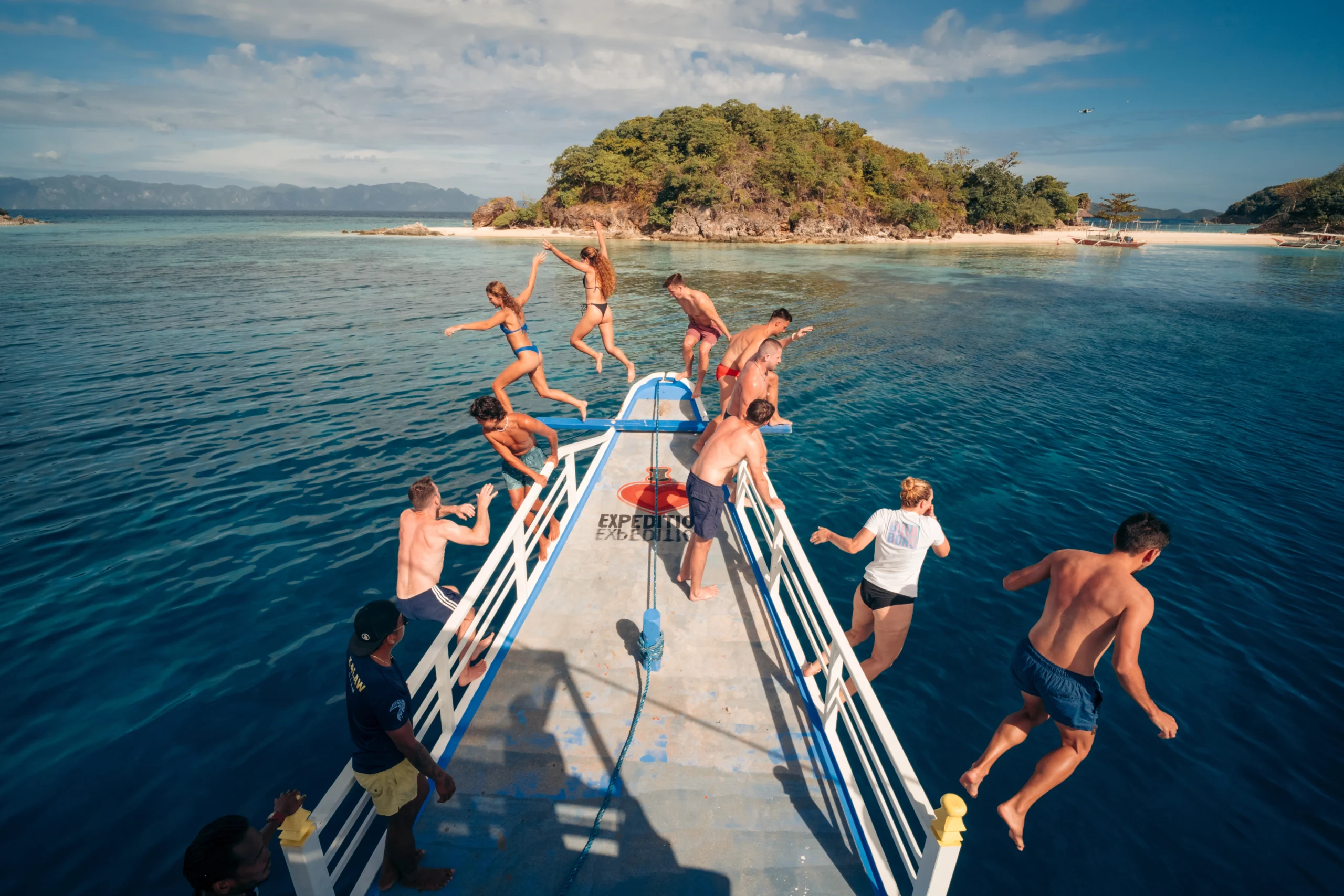 Travelers jumping off the bow of a boat into crystal clear waters during a 3-day Palawan island hopping adventure.