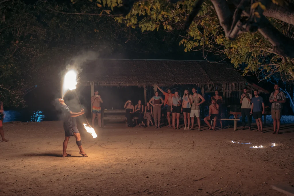 Tourists watching a local fire dancer perform on the beach at night during a Palawan island expedition basecamp stay.