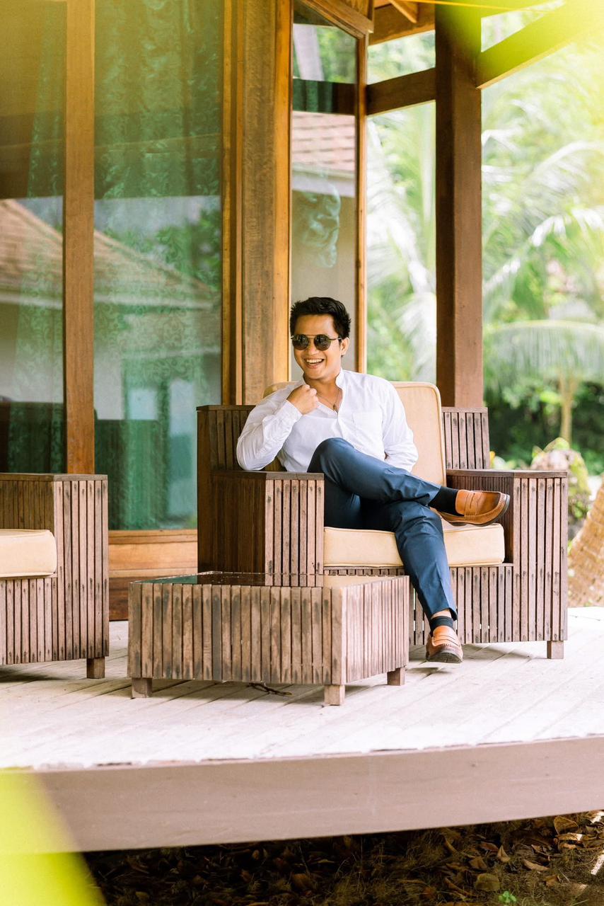 Jovet Rosento, founder of Yohak Tours, smiling while relaxing in a premium wooden lounge chair on a sunlit tropical deck.