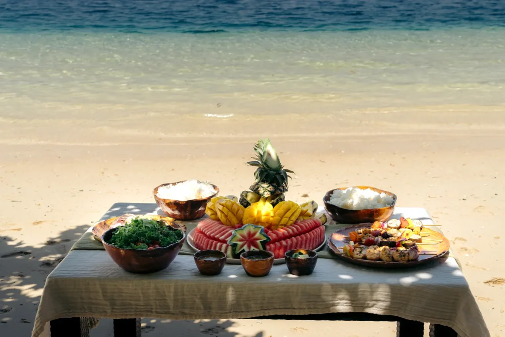 A private island lunch setup featuring fresh grilled seafood, rice, salad, and tropical fruits like mango and watermelon in Palawan.
