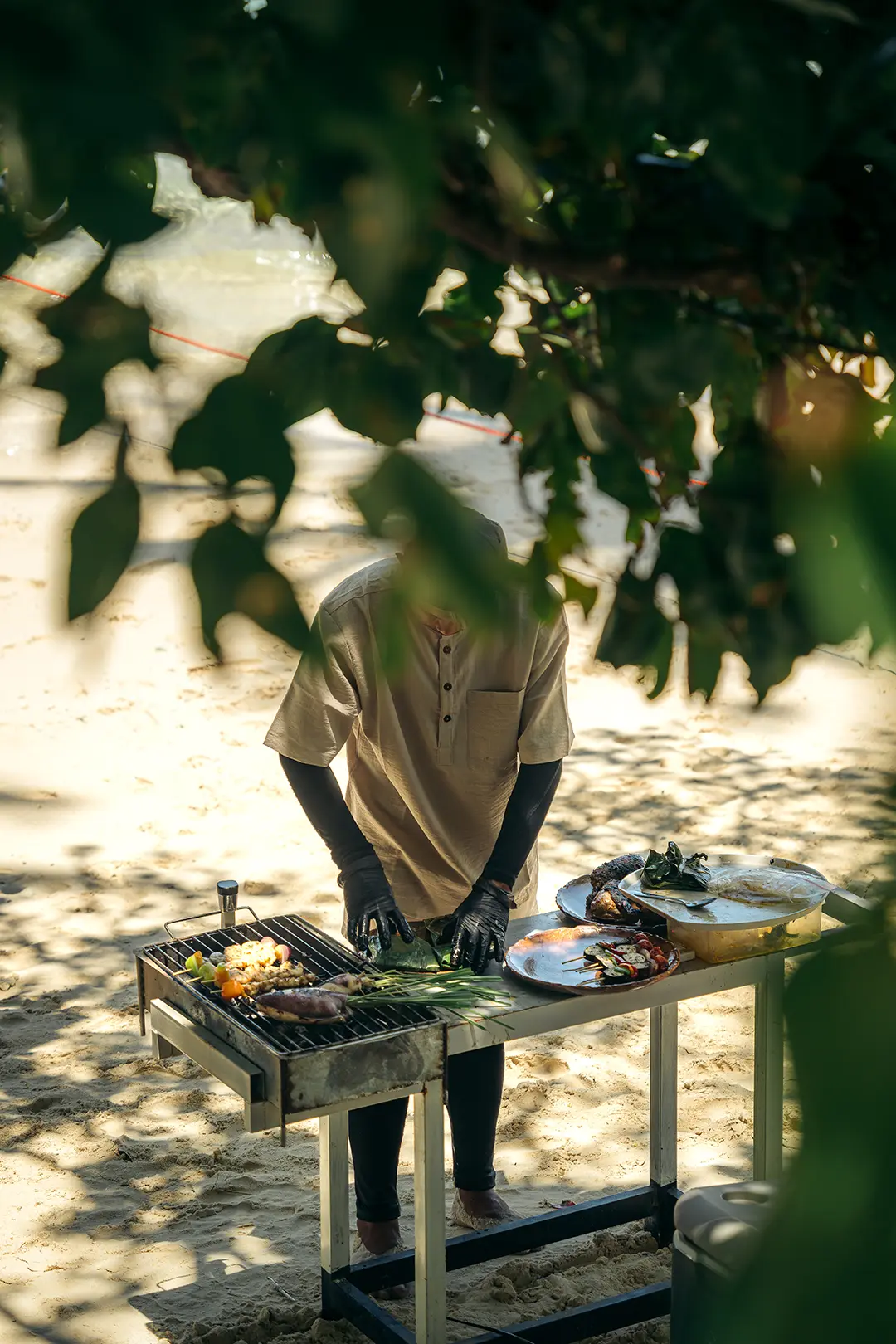 A private tour chef in uniform grilling fresh seafood and vegetables on a portable grill on a white sand beach in Palawan.