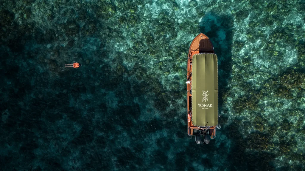 Aerial view of a swimmer approaching the YOHAK luxury speedboat in El Nido's coral-filled waters.