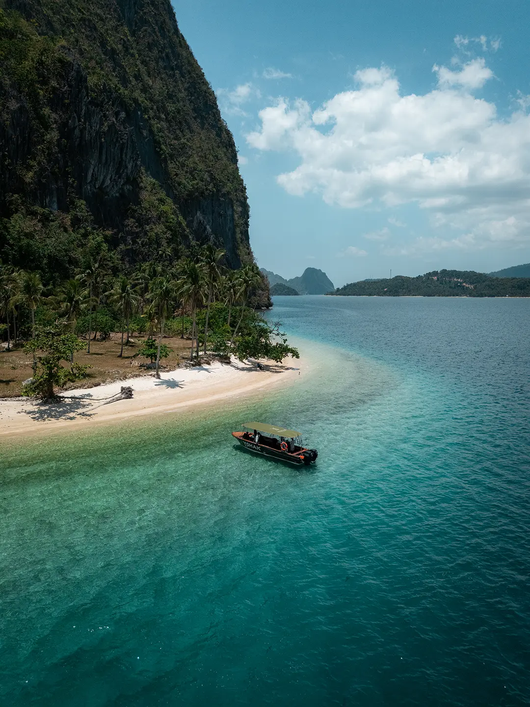 yohak-luxury-seascape-expedition-palawan Aerial landscape of a sweeping El Nido bay with distant islands and the Yohak boat anchored near the shore.
