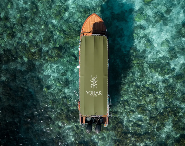 A top-down drone view of a luxury Yohak speedboat anchored in the clear, coral-filled waters of El Nido, Palawan.