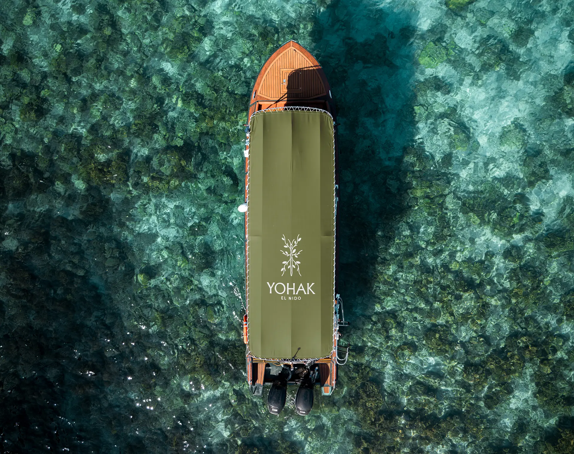 A top-down drone view of a luxury Yohak speedboat anchored in the clear, coral-filled waters of El Nido, Palawan.