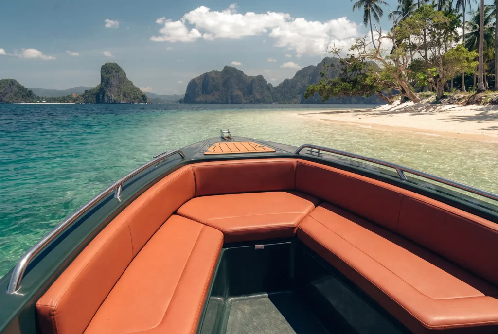 Spacious brown cushioned seating inside a Yohak speedboat overlooking turquoise water, white sand beach, and limestone islands in El Nido.
