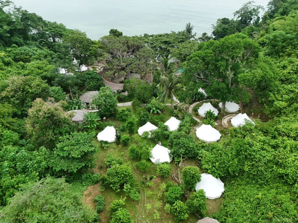 Aerial view of Parada Beach Camp with white glamping tents surrounded by lush tropical forest beside the sea.