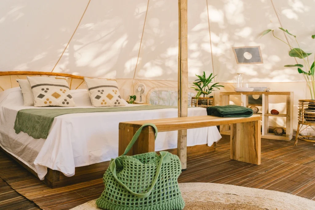 Glamping bell tent interior with bed wooden bench and green accents at Parada Beach Camp