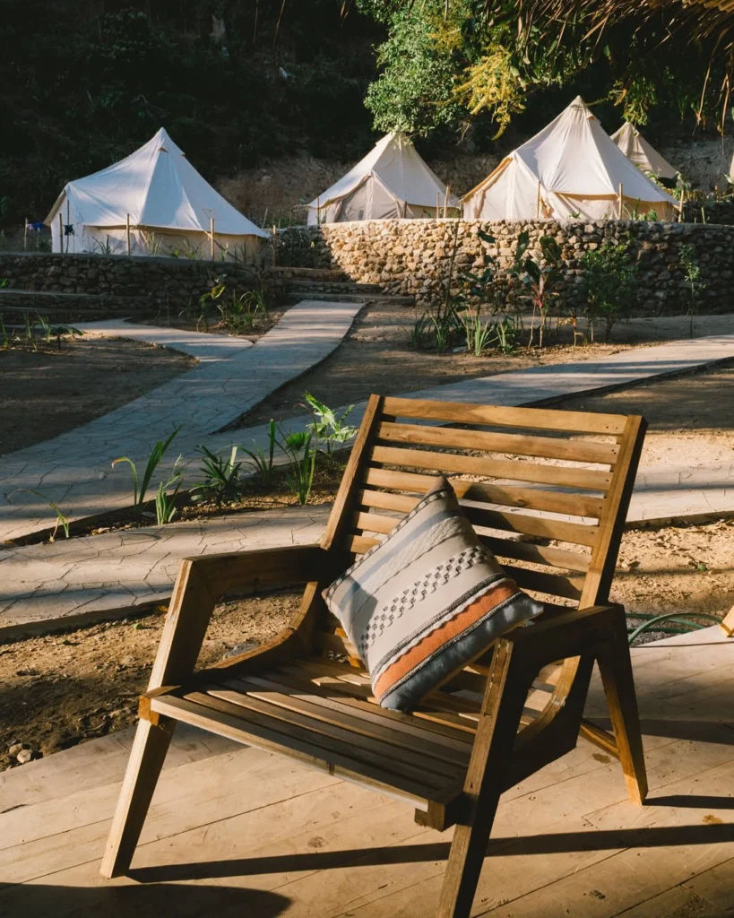 Wooden lounge chair overlooking terraced glamping tents at Parada Beach Camp Linapacan